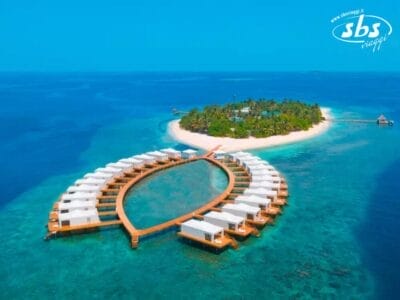 Vista aerea dei bungalow sull'acqua, che formano una mezzaluna attorno a una piccola isola tropicale, con vegetazione lussureggiante e acque cristalline dell'oceano: la cornice perfetta per Bozza automatica.