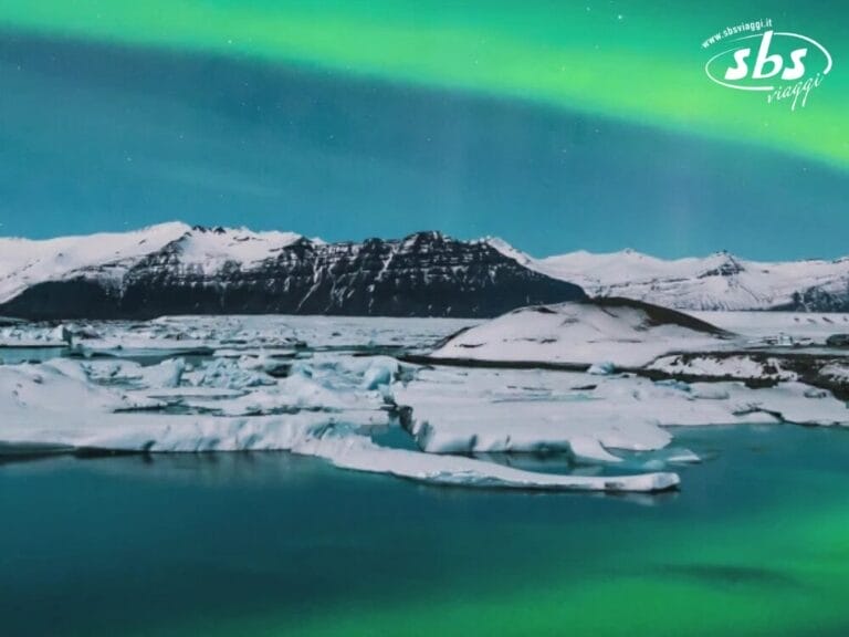 L'aurora boreale danza sul paesaggio ghiacciato dell'Islanda, con montagne maestose e uno specchio d'acqua calmo che riflette i suoi colori vivaci.