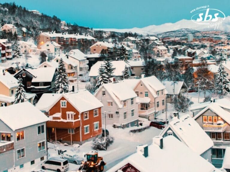 Nel quartiere residenziale innevato di Tromso, dove case e alberi si annidano sotto una coltre bianca incontaminata, un trattore sgombera diligentemente la strada. Questo paesaggio artico offre uno sfondo sereno, illuminato occasionalmente dalla danza ipnotizzante dell'aurora boreale.