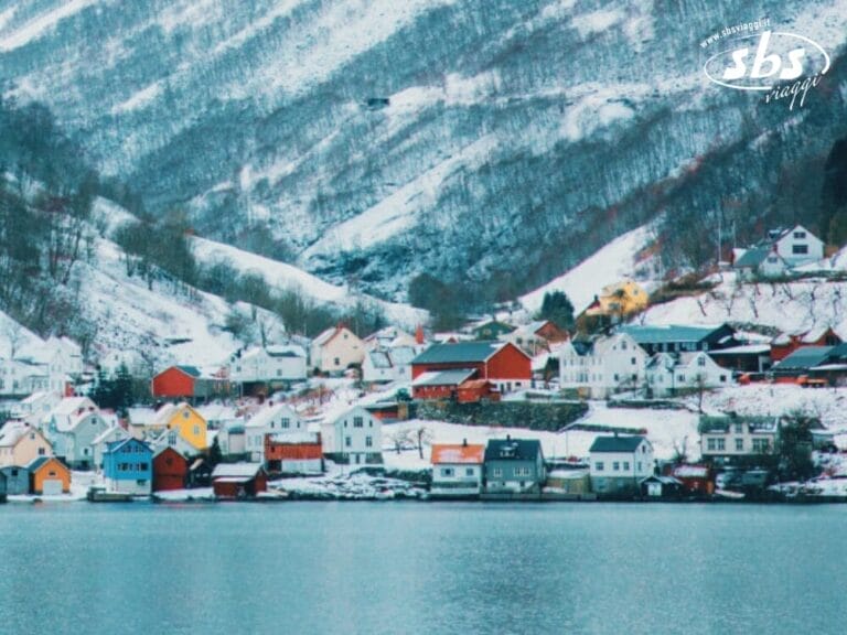 Una cittadina con case colorate in riva a un lago, circondata da colline innevate, offre uno scenario pittoresco che ricorda i fiordi nordici, perfetto per una magica festa di Capodanno.