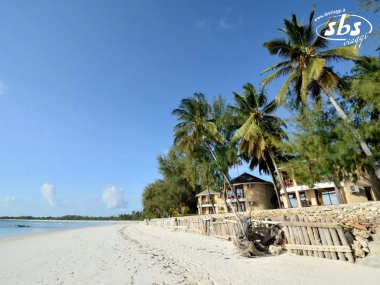 Spiaggia sabbiosa con alte palme, recinzioni in legno e graziosi edifici vicino alla riva, sotto un cielo azzurro e limpido, che ricorda l'atmosfera serena di Kae Beach.