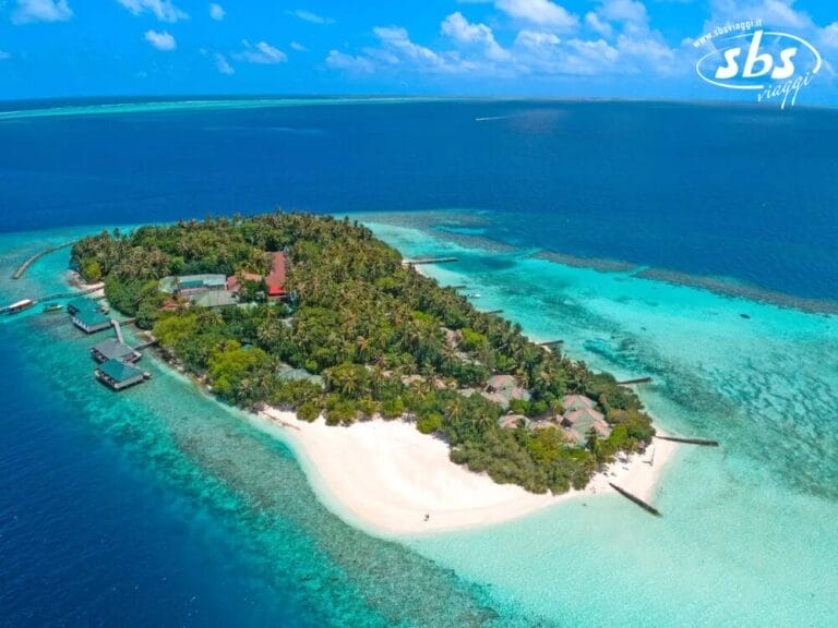 Vista aerea della lussureggiante isola tropicale di Embudu, sede del Village Island Resort, circondata da acque oceaniche turchesi e blu intenso, con spiagge di sabbia bianca e incantevoli strutture sull'acqua.