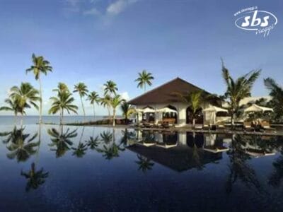 Una fuga tropicale vi attende nel resort di lusso, caratterizzato da palme e un edificio con tetto di paglia che si riflette in una piscina tranquilla. Immergetevi nella bellezza serena del Residence Zanzibar e vivete il paradiso.