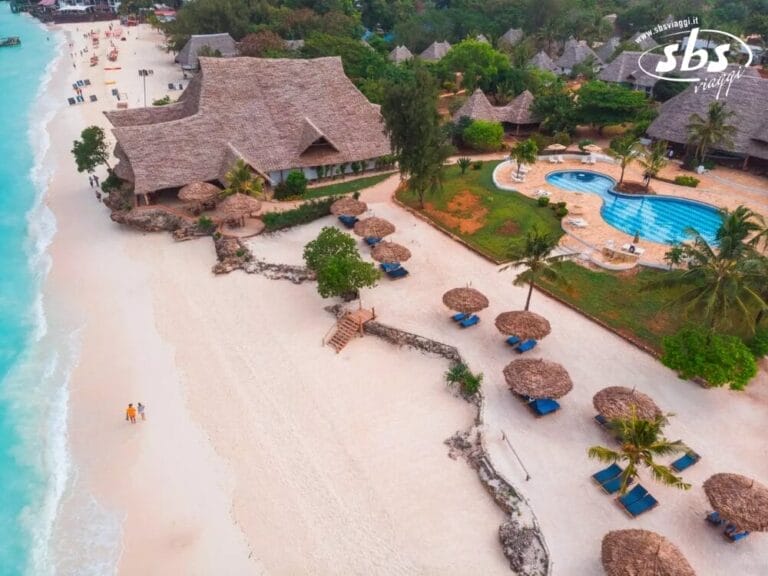 Vista aerea del resort Seaclub Sandies Baobab, con edifici dal tetto di paglia, una piscina e ombrelloni che costeggiano la riva, accanto alle acque turchesi dell'oceano.