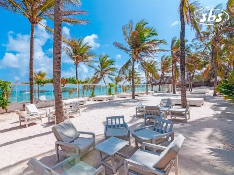 L'area lounge Beachside del Barracuda Inn vanta sabbia bianca, sedie a sdraio sparse, tavoli e palme ondeggianti. Gli ospiti possono godere di viste mozzafiato sull'oceano sotto un cielo azzurro e limpido in questo tranquillo resort sulla spiaggia.