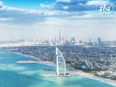 Vista aerea che mette in mostra la bellezza inconfondibile di Dubai con l'iconico Burj Al Arab, uno skyline cittadino mozzafiato e una costa pittoresca sotto un cielo parzialmente nuvoloso.