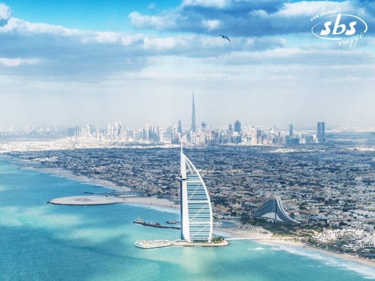 Vista aerea che mette in mostra la bellezza inconfondibile di Dubai con l'iconico Burj Al Arab, uno skyline cittadino mozzafiato e una costa pittoresca sotto un cielo parzialmente nuvoloso.