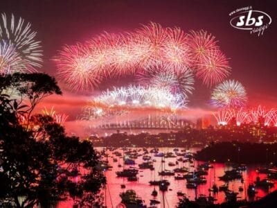 I fuochi d'artificio illuminano il cielo sopra il porto di Sydney, riflettendosi sull'acqua con le barche in primo piano, ricordando una sfavillante celebrazione di Capodanno.