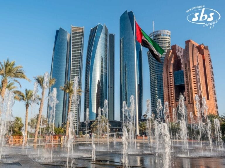 Una fontana con getti d'acqua impreziosisce il primo piano, mentre maestosi grattacieli e una bandiera degli Emirati Arabi Uniti sventolano orgogliosi sullo sfondo sotto un cielo azzurro e limpido, catturando le meraviglie degli Emirati Arabi Uniti moderni.