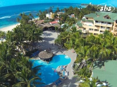 Vista aerea del Coral Costa Caribe, un lussuoso resort sulla spiaggia dotato di una scintillante piscina incastonata tra palme ondeggianti ed eleganti edifici, il tutto sullo sfondo mozzafiato di una spiaggia incontaminata e di un oceano cristallino.