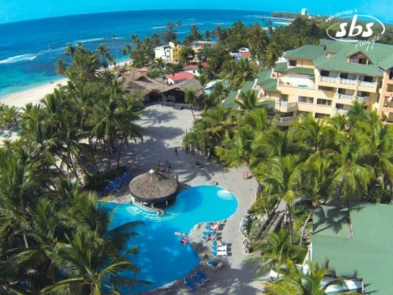 Vista aerea del Coral Costa Caribe, un lussuoso resort sulla spiaggia dotato di una scintillante piscina incastonata tra palme ondeggianti ed eleganti edifici, il tutto sullo sfondo mozzafiato di una spiaggia incontaminata e di un oceano cristallino.