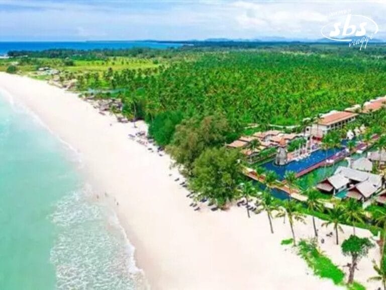 Vista aerea di un resort sulla spiaggia thailandese con sabbia bianca e acqua turchese, fiancheggiato da palme e dagli eleganti edifici del resort Kappa Club.