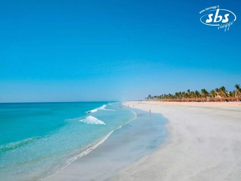 L'ampia spiaggia sabbiosa, con le sue acque turchesi sotto un cielo azzurro e limpido, fiancheggiata da palme e lambita dalla magia della bozza automatica, rivela uno scenario tranquillo, dove solo pochi passeggiatori passeggiano lungo la riva serena.