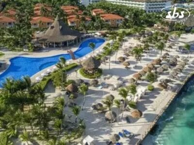 Da una vista aerea, il resort tropicale mette in mostra una piscina serpentina fiancheggiata da ombrelloni di paglia e palme ondeggianti. Questa cornice idilliaca, completa di una spiaggia sabbiosa che si fonde perfettamente con l'oceano, sembra semplice come una bozza automatica.