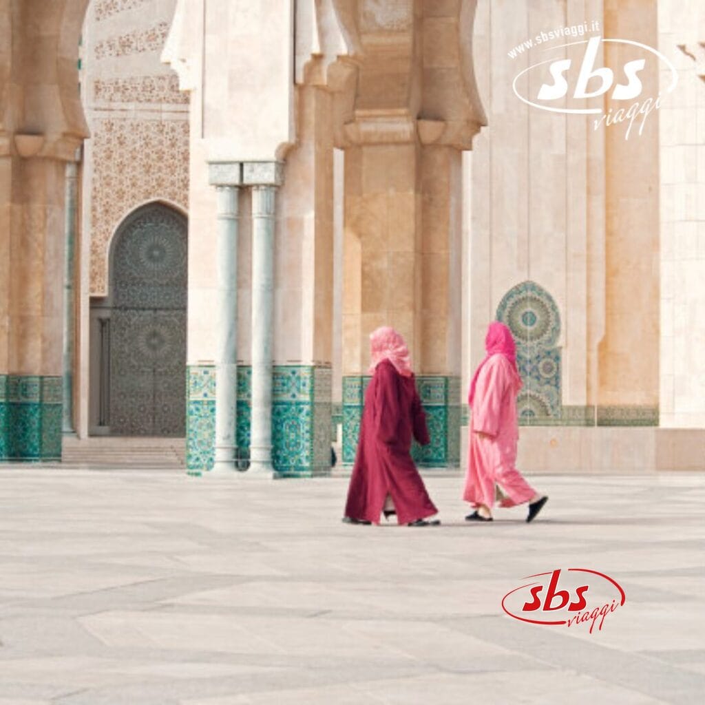 Due persone in abiti colorati passeggiano in un cortile decorato con archi e piastrelle decorate, catturando la vivace essenza della medina del Nord del Marocco.