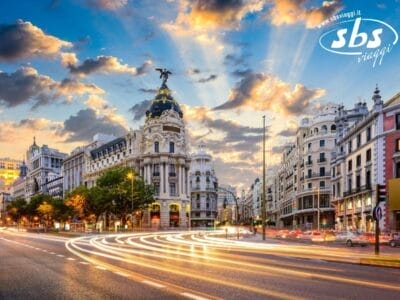 Una vivace strada di Madrid con edifici storici e un tramonto spettacolare, con scie luminose lasciate dai veicoli in transito.