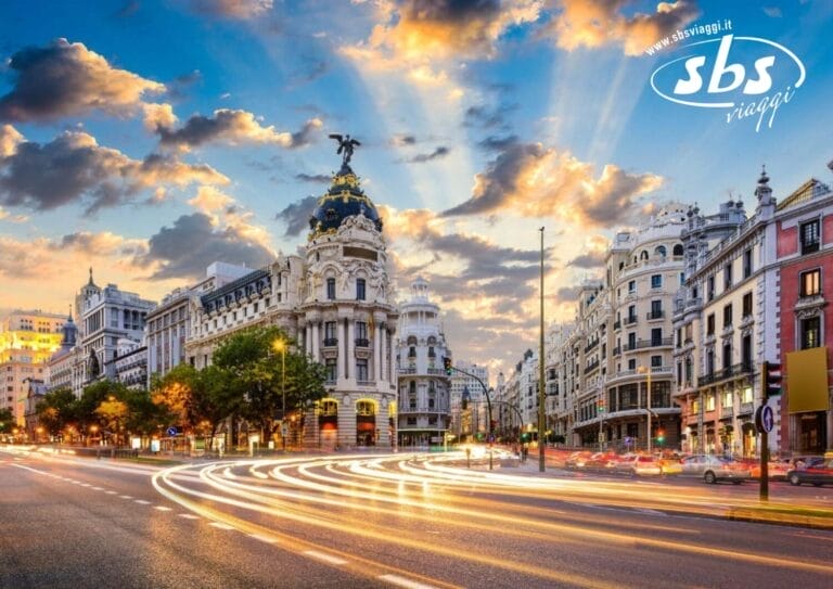 Una vivace strada di Madrid con edifici storici e un tramonto spettacolare, con scie luminose lasciate dai veicoli in transito.