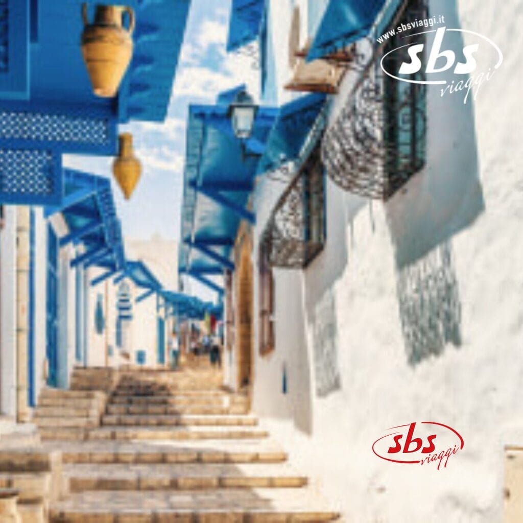 Una stretta strada in Tunisia con edifici bianchi e dettagli blu, caratterizzata da gradini che salgono e lanterne decorative appese in alto.