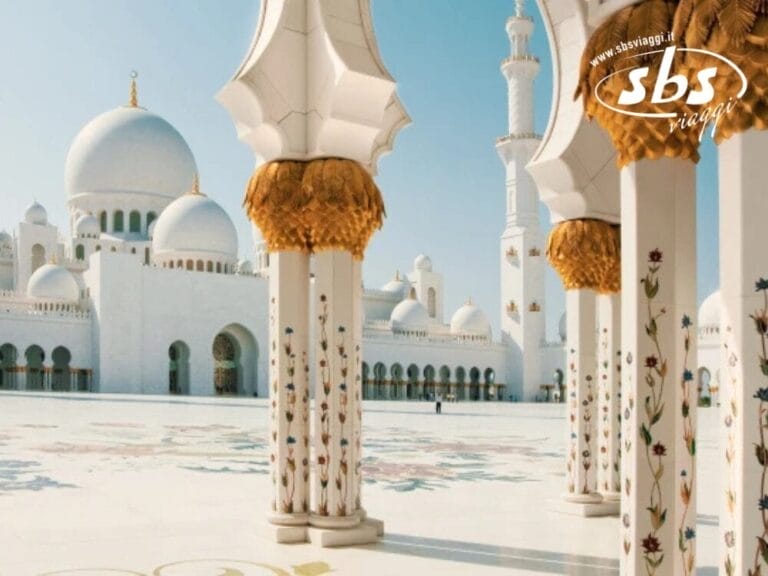 Vista del cortile di una moschea con colonne bianche decorate e cupole sotto il cielo limpido di Abu Dhabi.