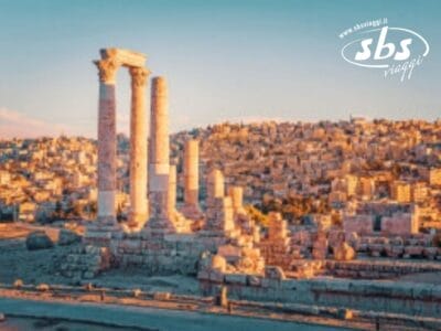 Antiche colonne di pietra si ergono fiere sotto un cielo limpido, incorniciando il paesaggio urbano della Giordania sullo sfondo. Una vera meraviglia, la scena cattura un mix senza tempo di storia e modernità.