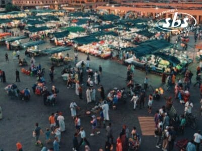 Vista aerea di un vivace mercato all'aperto di Marrakech, con numerose bancarelle e molte persone che passeggiano.