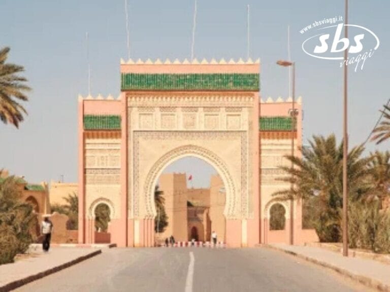 Un arco decorato con intricati disegni si erge all'ingresso di una strada fiancheggiata da palme, sotto un cielo limpido, riecheggiando la magnificenza della Città Imperiali.