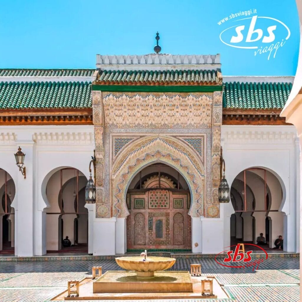 L'immagine ritrae un ingresso decorato ad arco di un tradizionale edificio islamico in Marocco, con motivi intricati e una fontana nel cortile, sotto un cielo azzurro e limpido: il momento clou del tuo tour.