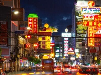 Una strada metropolitana movimentata di notte, illuminata da vivaci insegne al neon in diverse lingue, tra cui il cinese. Sotto un cielo scuro, auto e pedoni scorrono in mezzo all'atmosfera vivace, catturando l'essenza di un dinamico paesaggio urbano cinese.