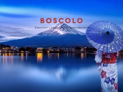 Una donna in kimono con ombrello di fronte al Monte Fuji, in riva a un lago al tramonto, con le luci della città che scintillano: un momento indimenticabile del Viaggio in Giappone.