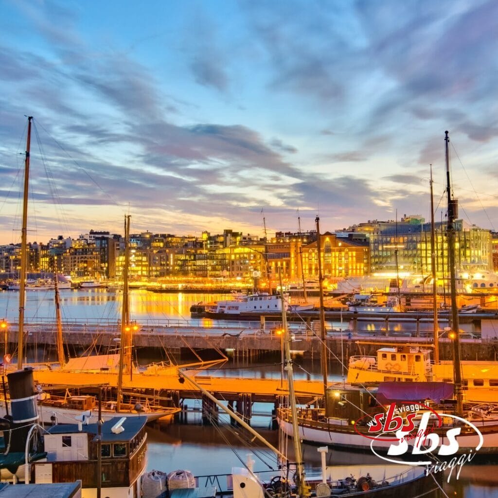 Barche attraccate in un porto al tramonto con gli edifici della città illuminati sullo sfondo: uno spettacolo che cattura la magia di ogni viaggio. Il logo 