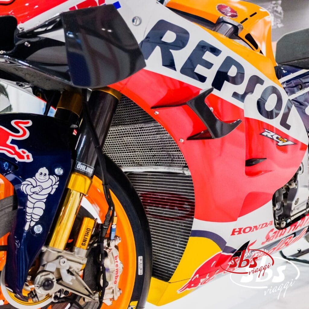 Primo piano della sezione anteriore di una moto da corsa Honda Repsol MotoGP, con in evidenza le ruote, le sospensioni e i loghi dettagliati degli sponsor.