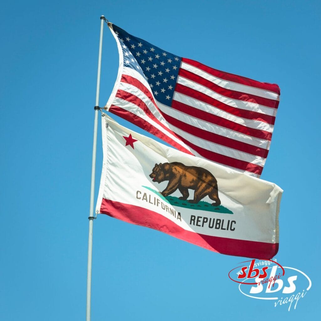 Due bandiere su pennoni contro un cielo azzurro: la bandiera degli Stati Uniti sopra la bandiera della Repubblica della California, a evocare l'orgoglio di Los Angeles, con il logo