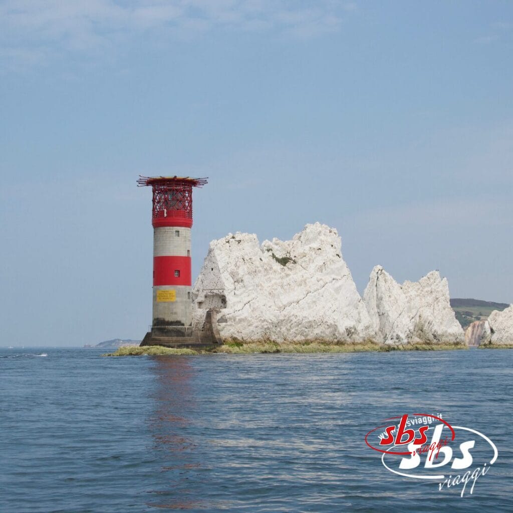Un faro a strisce rosse e bianche si erge su una formazione rocciosa circondata da un mare calmo sotto un cielo limpido, offrendo una vista pittoresca tipica delle Isole Scozia e una tappa popolare durante un Tour Scozia.