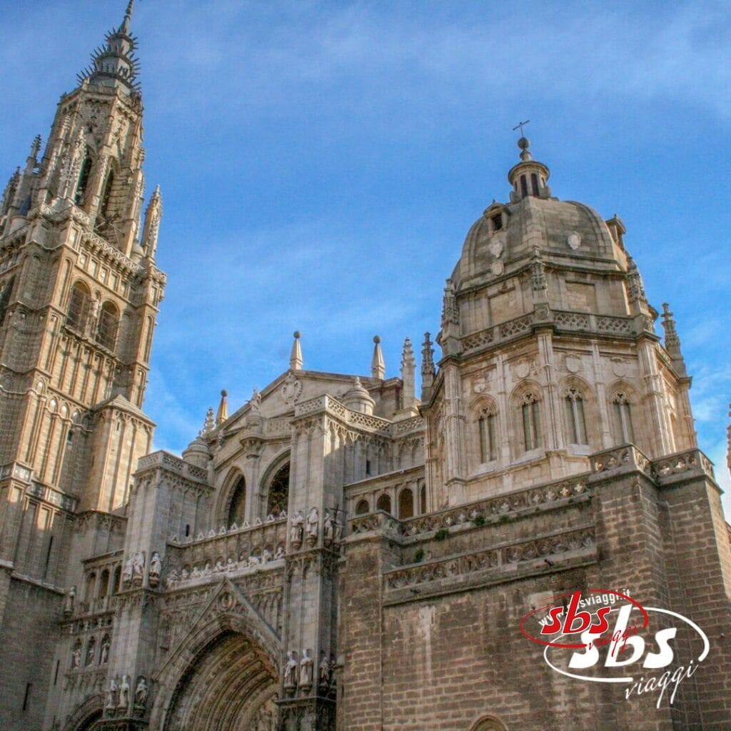 Vivi il tour di una cattedrale gotica con guglie e archi decorati che si stagliano contro un cielo azzurro, catturando le meraviglie della Spagna Medievale. Il logo di SBS Viaggi campeggia elegantemente nell'angolo in basso a destra, aggiungendo un tocco di distinzione.