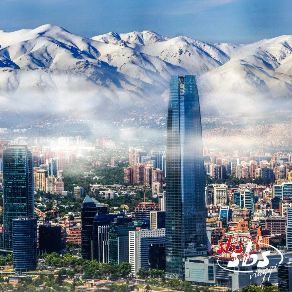 Un paesaggio urbano con alti grattacieli moderni di fronte alle montagne innevate della Patagonia, parzialmente coperto da un sottile strato di nebbia. Il logo