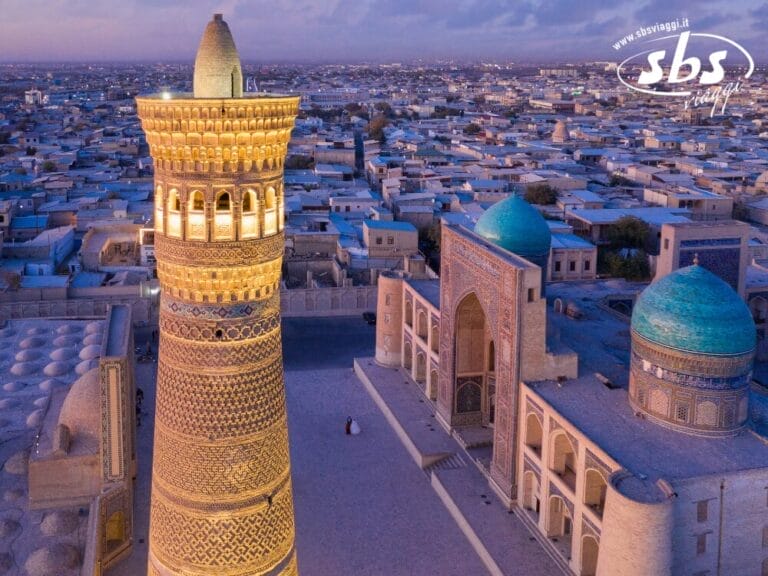 Vista aerea del minareto Kalyan illuminato e dei vicini edifici con le cupole blu a Bukhara, in Uzbekistan: un'immagine iconica nel cuore della Terra di Tamerlano, con un vasto paesaggio urbano sullo sfondo.