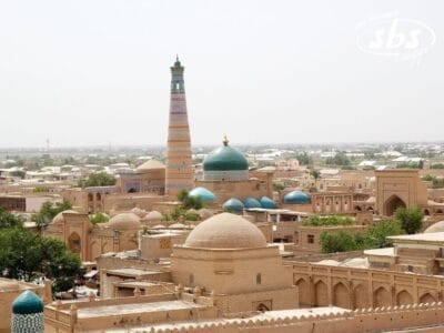 Una vista panoramica di Khiva, in Uzbekistan, nella Terra di Tamerlano, che mostra storici edifici in mattoni di fango, cupole turchesi e l'alto minareto decorato di Kalta Minor sotto un cielo limpido.