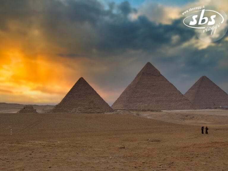 Tre piramidi si ergono su una pianura sabbiosa sotto un cielo spettacolare al tramonto, vicino al Cairo, con due persone visibili in lontananza.