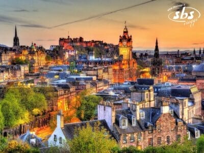 Una vista panoramica di Edimburgo al tramonto, con edifici storici, la torre dell'orologio di Balmoral illuminata e l'iconico castello di Edimburgo su una collina: un momento indimenticabile di qualsiasi Tour Scozia.