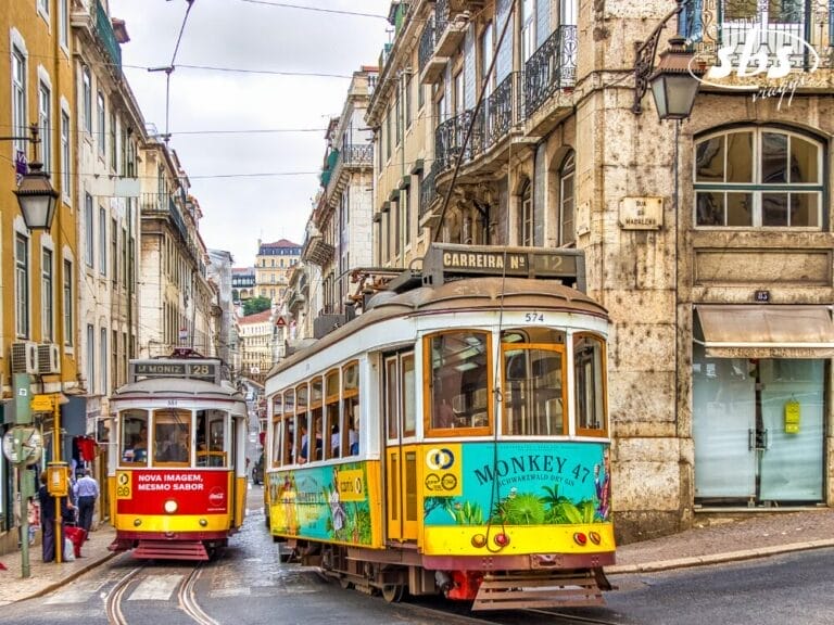 Due tram d'epoca percorrono i binari di una stretta strada fiancheggiata da vecchi edifici a Lisbona, in Portogallo, e le loro pubblicità colorate aggiungono fascino: uno scenario autentico, perfetto per un Tour Portogallo.