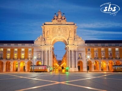 L'arco illuminato di Rua Augusta a Lisbona, in Portogallo, si erge tra due edifici storici al tramonto, mentre i lampioni si accendono e passa un tram: lo scenario perfetto per un'esperienza Tour Cocktail Portoghese.