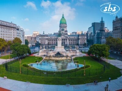Vista grandangolare del palazzo del Congresso Nazionale Argentino con una grande statua e una fontana in primo piano, circondato da prati verdi e palazzi cittadini: uno scenario iconico da ammirare durante la tua avventura nel Tour Argentina.
