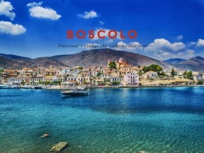 Colorata cittadina di mare con barche, montagne sullo sfondo e un nuotatore nel mare blu; il testo recita "BOSCOLO".
