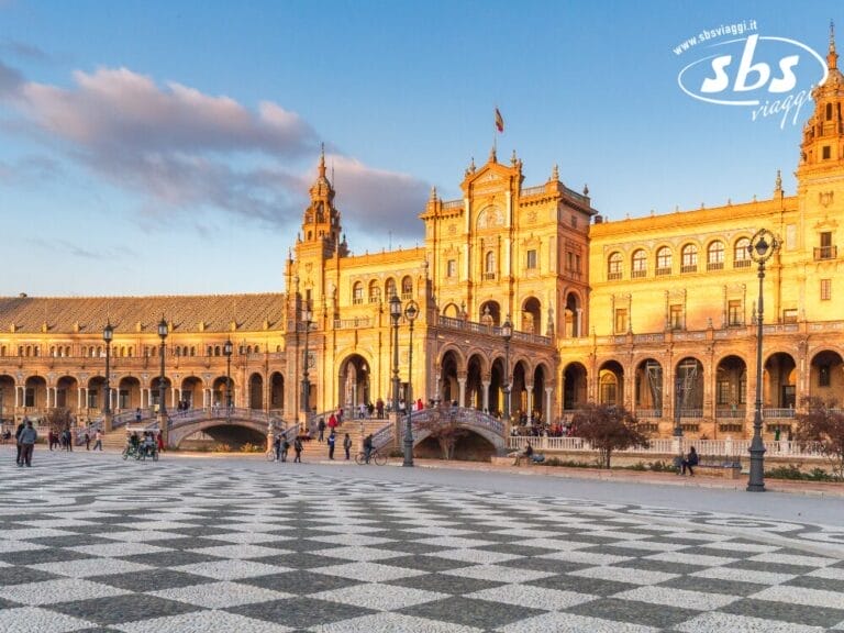 Plaza de España a Siviglia, tappa obbligata di qualsiasi tour dell'Andalusia, è caratterizzata da un edificio decorato con ponti ad arco che si stagliano contro un cielo azzurro. In primo piano, un intricato motivo a scacchiera incanta ogni visitatore.