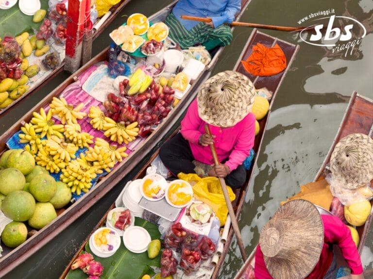 Vista aerea di venditori con cappelli che propongono frutta e cibo da barche di legno in un vivace mercato galleggiante: un momento imperdibile di qualsiasi esperienza del Tour Thailandia.