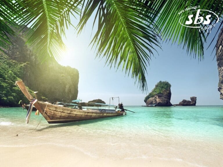 Una barca di legno è ormeggiata su una spiaggia tropicale sabbiosa con acque limpide e turchesi e scogliere rocciose, incorniciate da foglie di palma, che catturano la serena bellezza di Koh Samui.