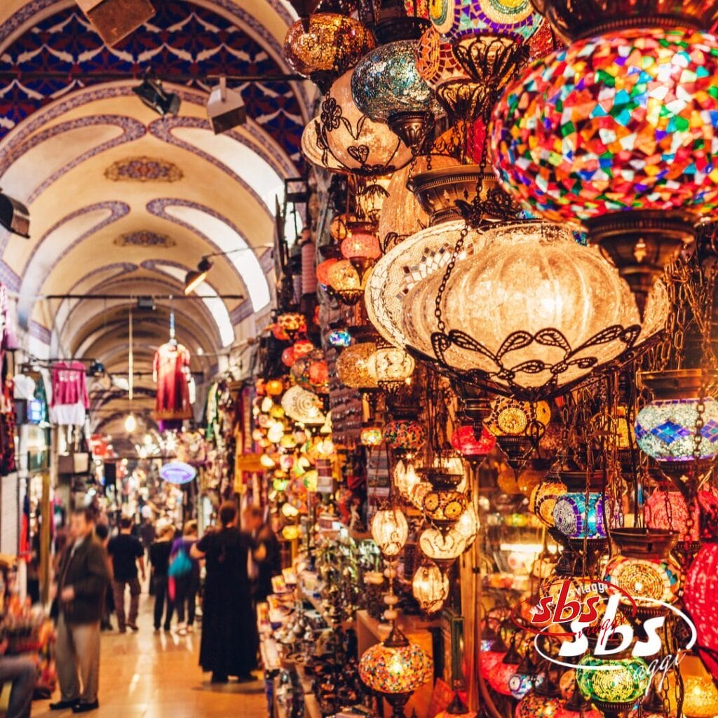 Lampade a mosaico colorate pendono dal soffitto di un bazar affollato e ad arco, mentre i clienti passeggiano nel vivace mercato: un'atmosfera che puoi sperimentare durante il tuo tour Istanbulissima o proseguendo il tuo viaggio nella magica Cappadocia.