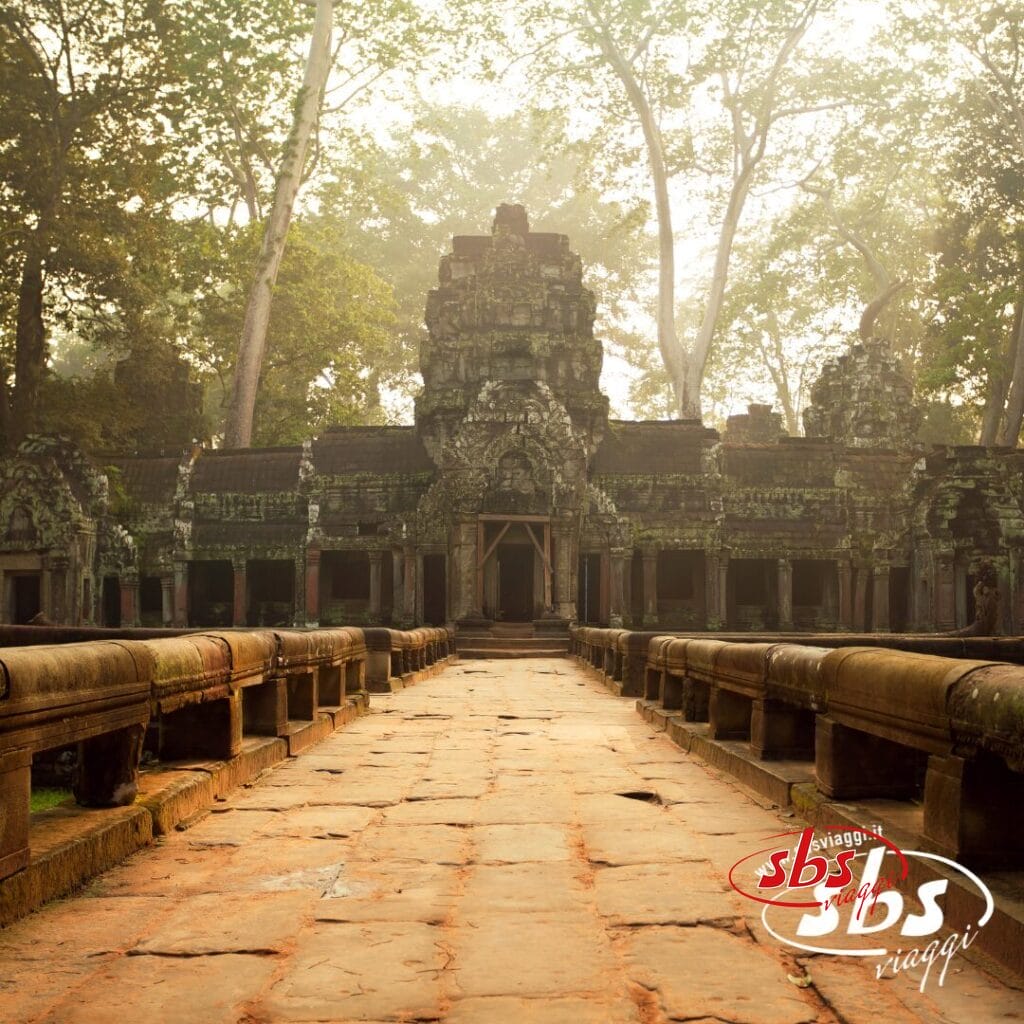Antico tempio in pietra con incisioni dettagliate, circondato da alberi e nebbia, visto da un sentiero che conduce all'ingresso. Il logo 