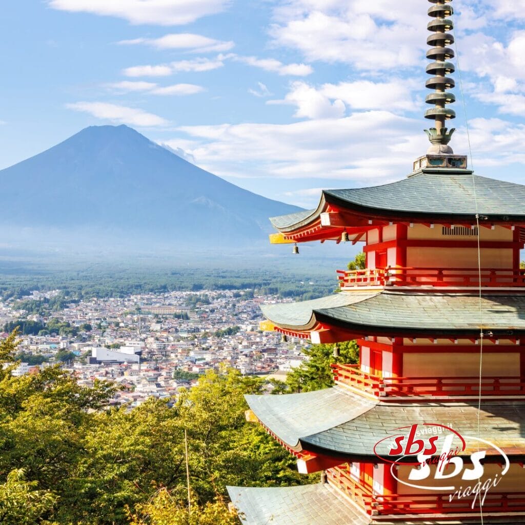 Pagoda rossa con una città e il Monte Fuji sullo sfondo, sotto un cielo parzialmente nuvoloso, che cattura lo spirito del Giappone. Il logo di SBS Viaggi è visibile nell'angolo in basso a destra.