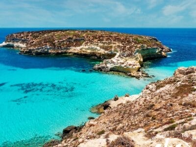 Costa rocciosa con acque turchesi e cristalline, una piccola isola e un cielo azzurro brillante: perfetta per una fuga rilassante vicino agli incantevoli villaggi o per un soggiorno tranquillo in hotel.
